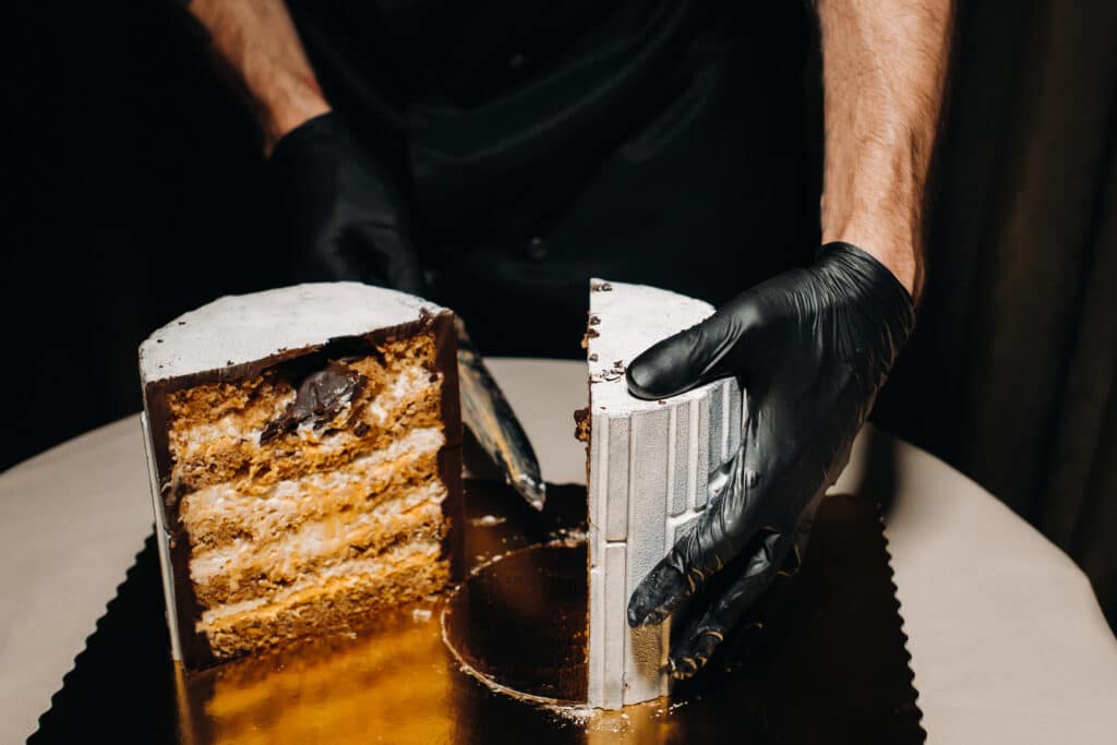 Amazing Cakes. A black-gloved chef is slicing a chocolate wedding cake. The wedding Cake is