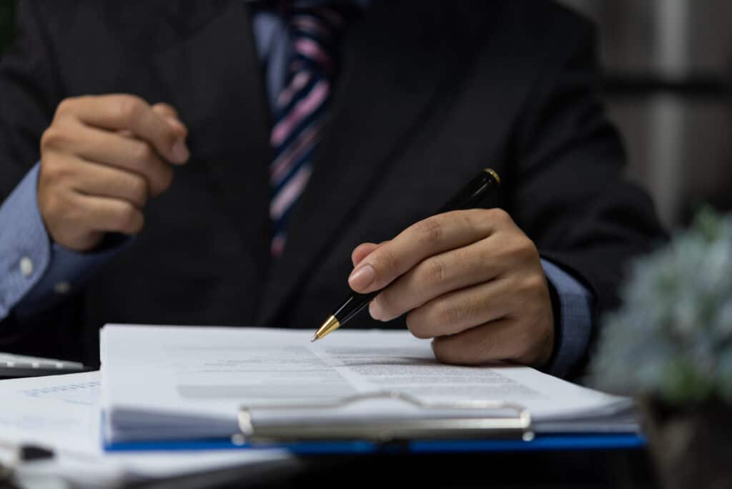 businessman holding pen signature document on clipboard at desk